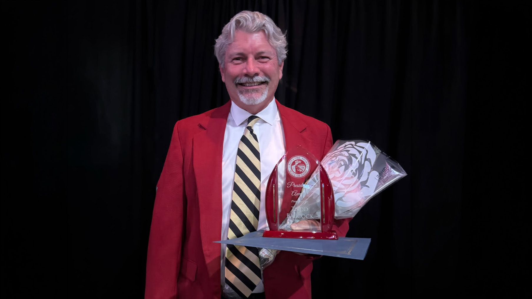 Man in a red coat smiles with award