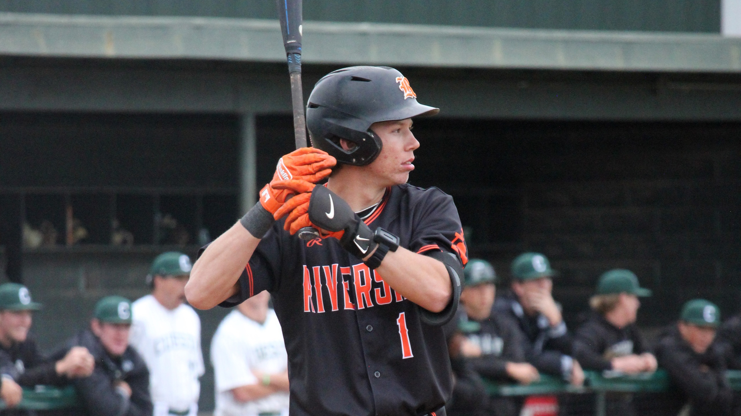 A baseball player in a black and orange uniform stands ready, holding a bat in a poised position.