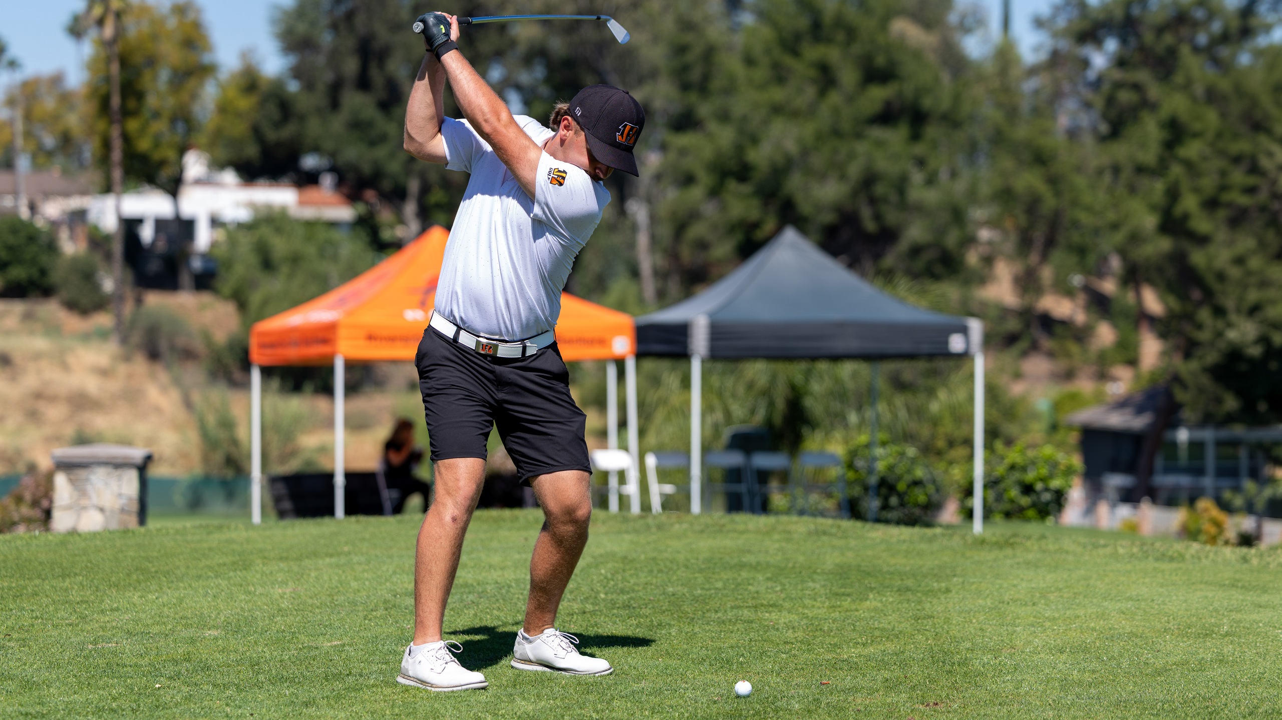 Men's golfer in white shirt gets ready to swing golf club.