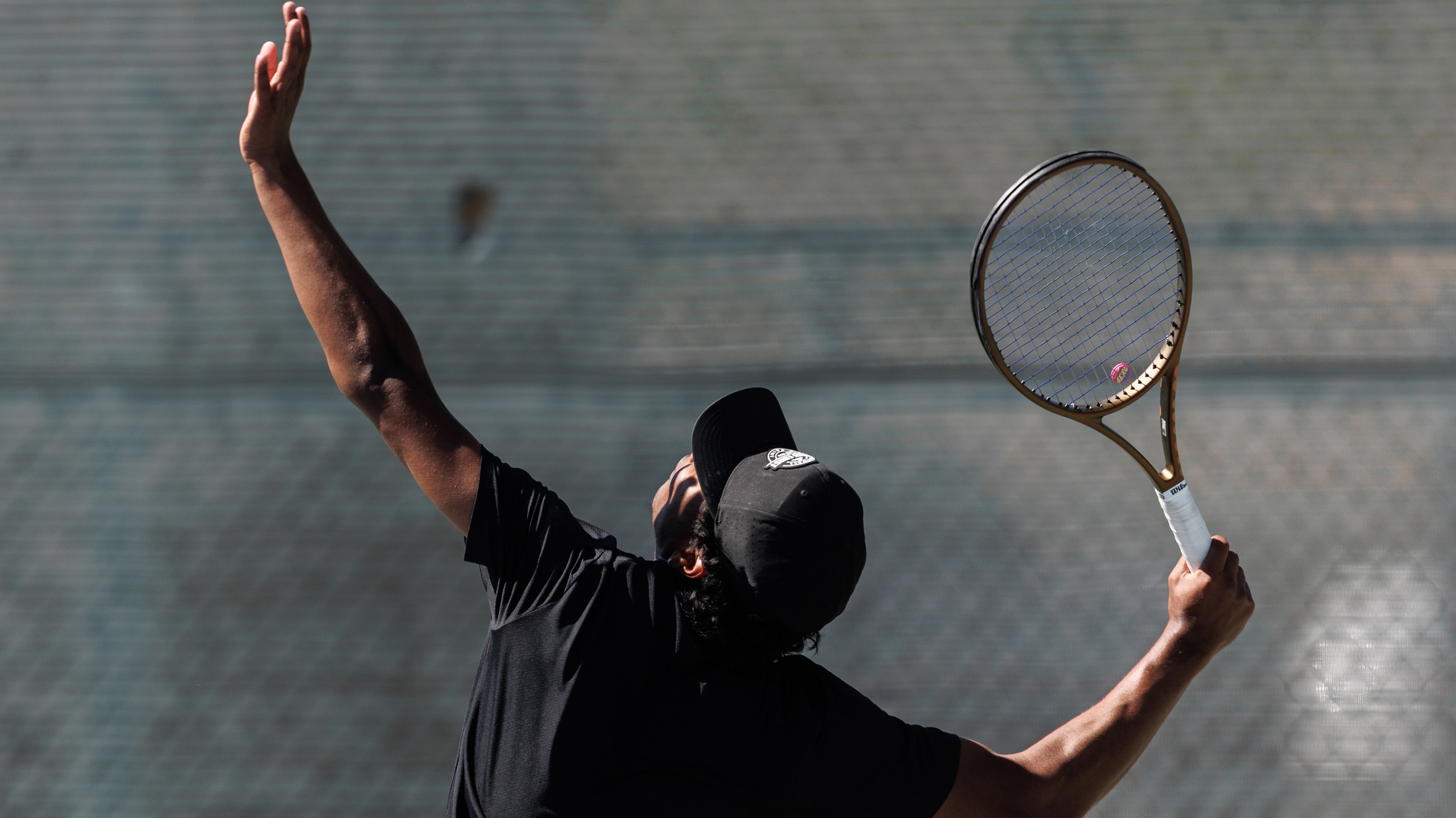 Men's tennis player in black outfit gets ready to serve.