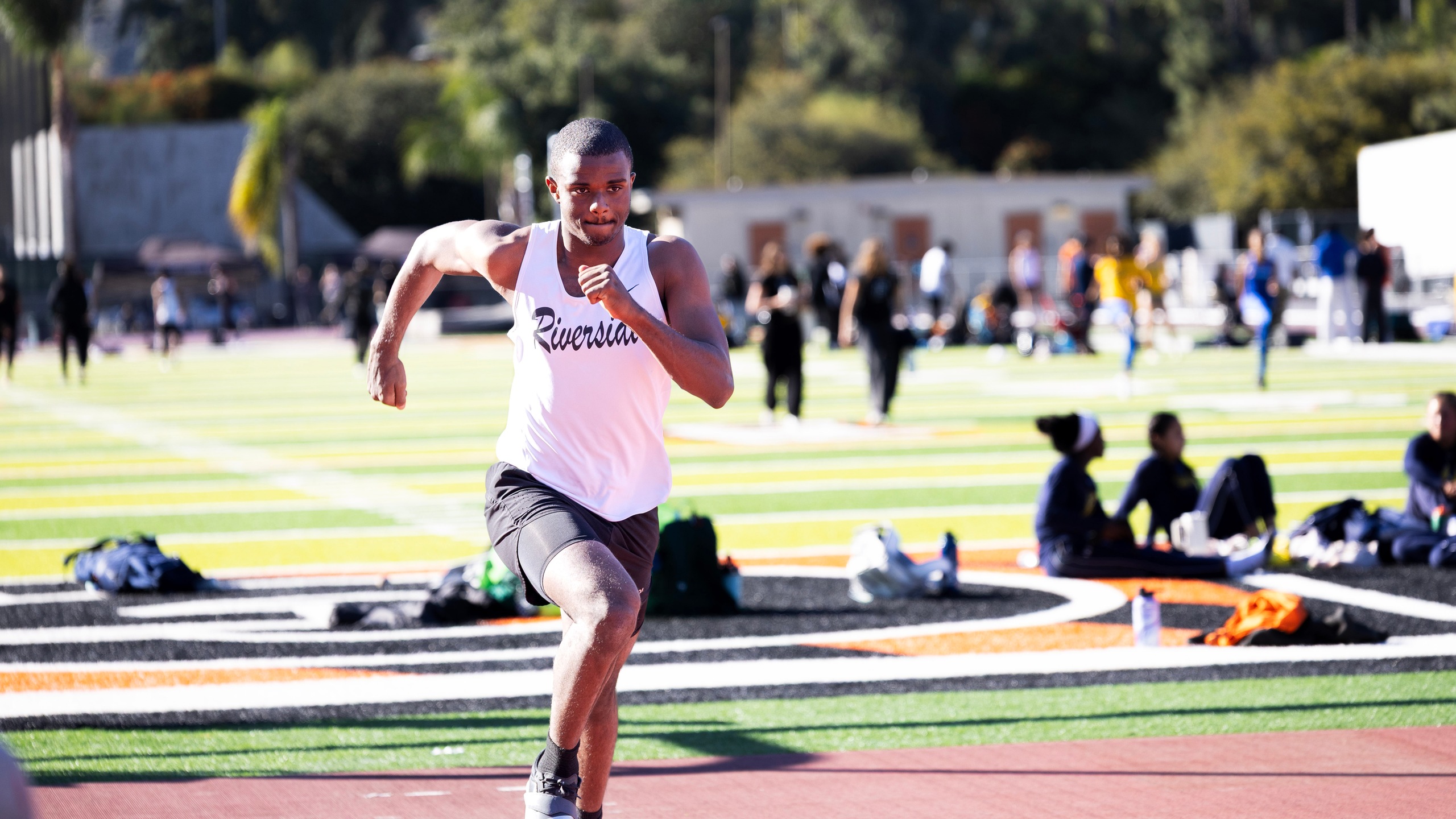 A young man sprinting on a track, with spectators watching from the sidelines.