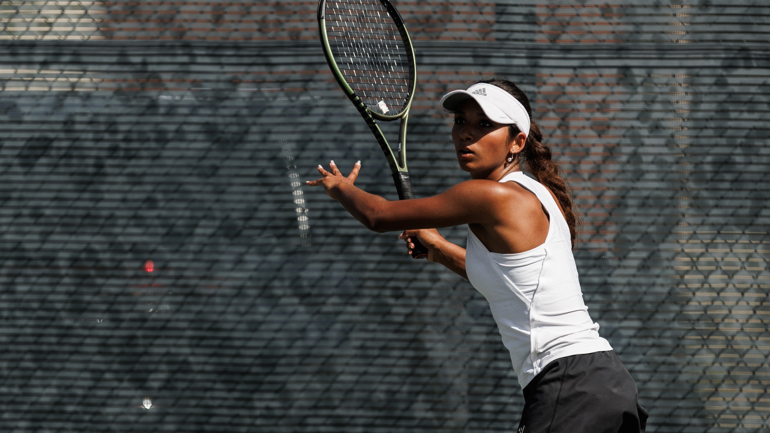 A women's tennis player in a white outfit gets ready to hit the ball