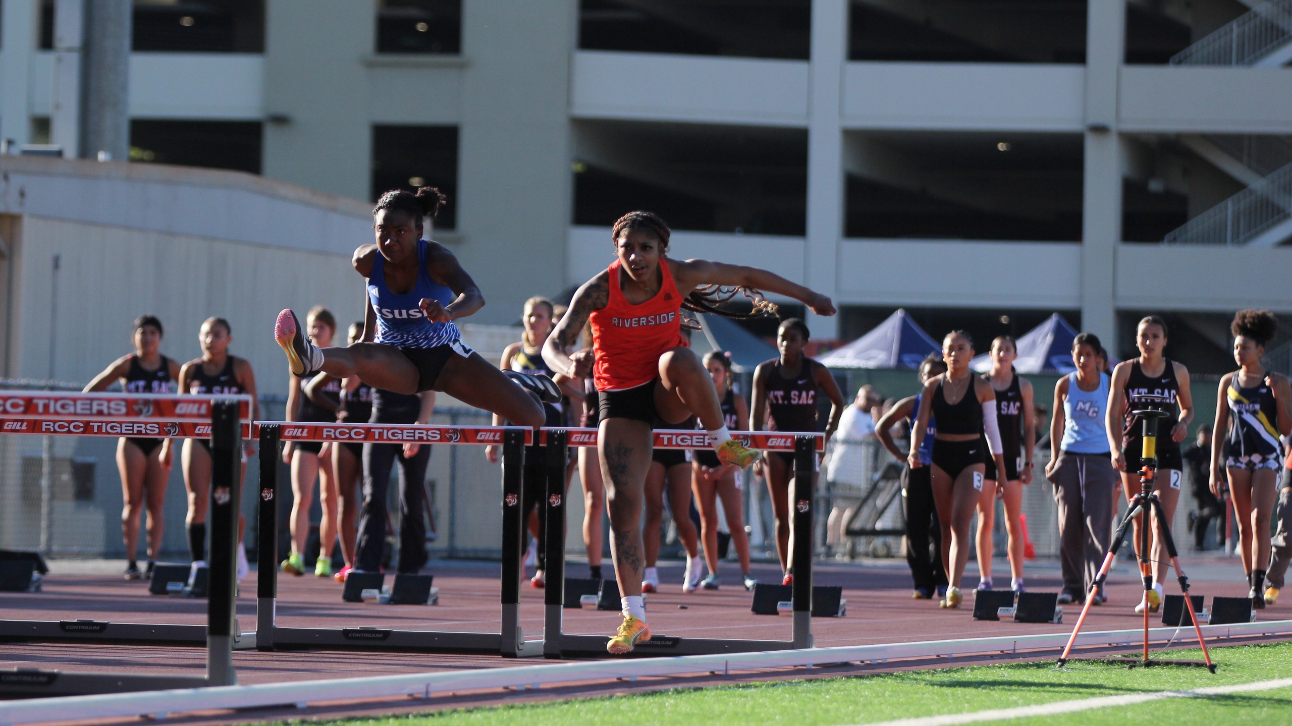 Two women athletes compete at a track meet, jumping over the hurdles